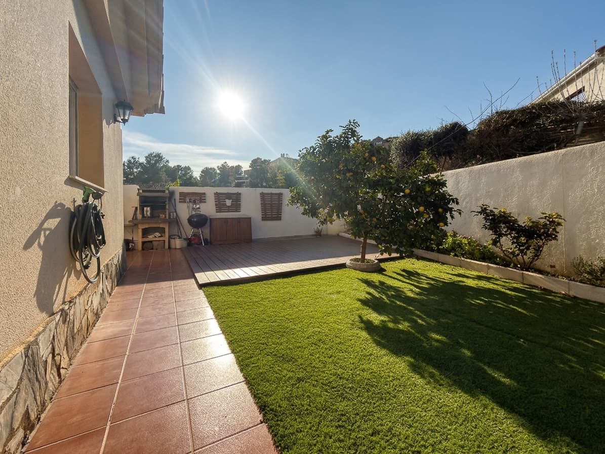 Jardín con césped y un naranjo bajo el sol de la tarde