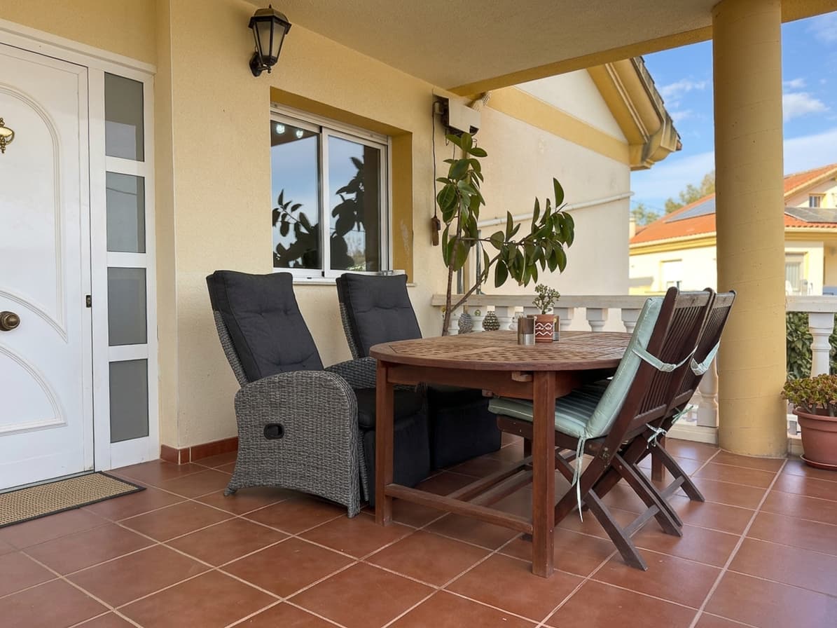 Porche soleado con una mesa de madera y sillas, preparado para comer fuera